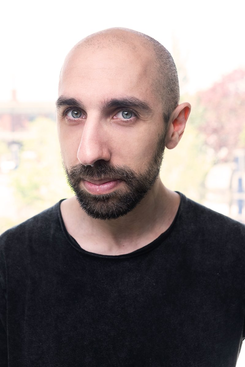 Jairus Khan, head and shoulders, in a black shirt against a bright window